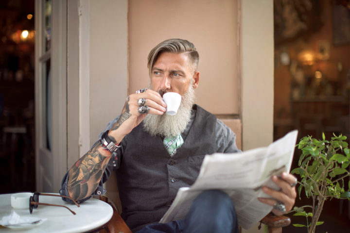 Mann sitzt im Cafe, liest Zeitung und trinkt Kaffee